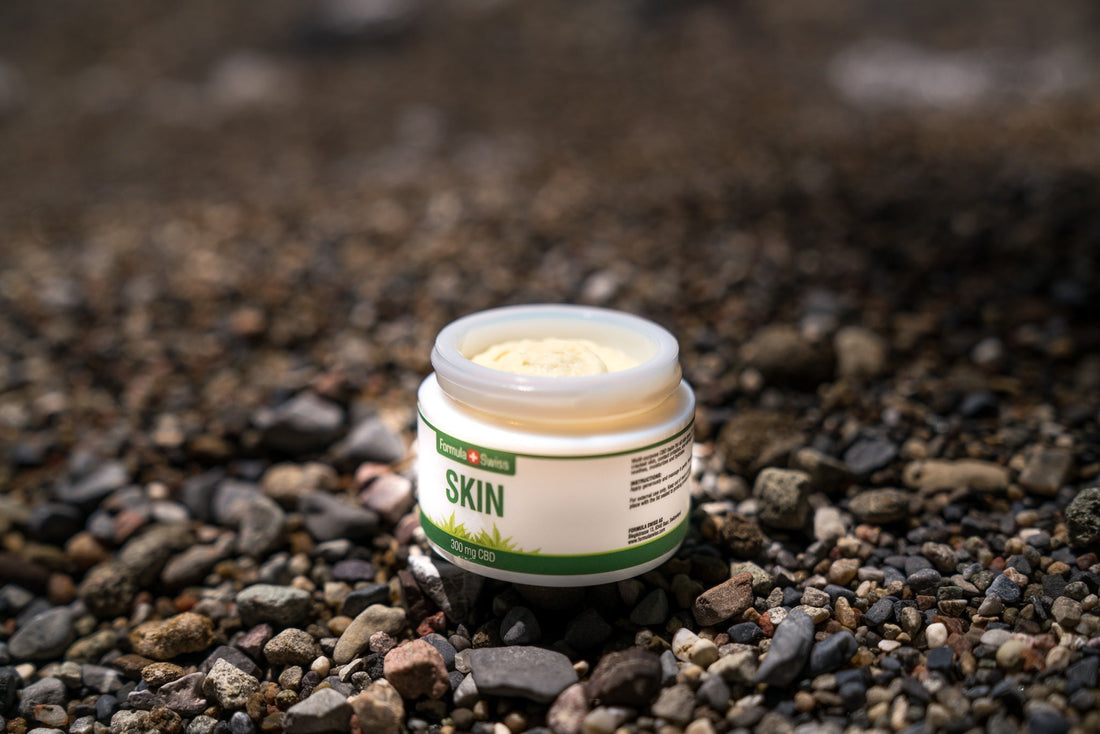 Borcan deschis de balsam Formula Swiss CBD Skin, 300 mg CBD, pe o plajă cu pietricele